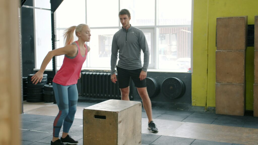 A person stepping onto a plyo box while another person stands by