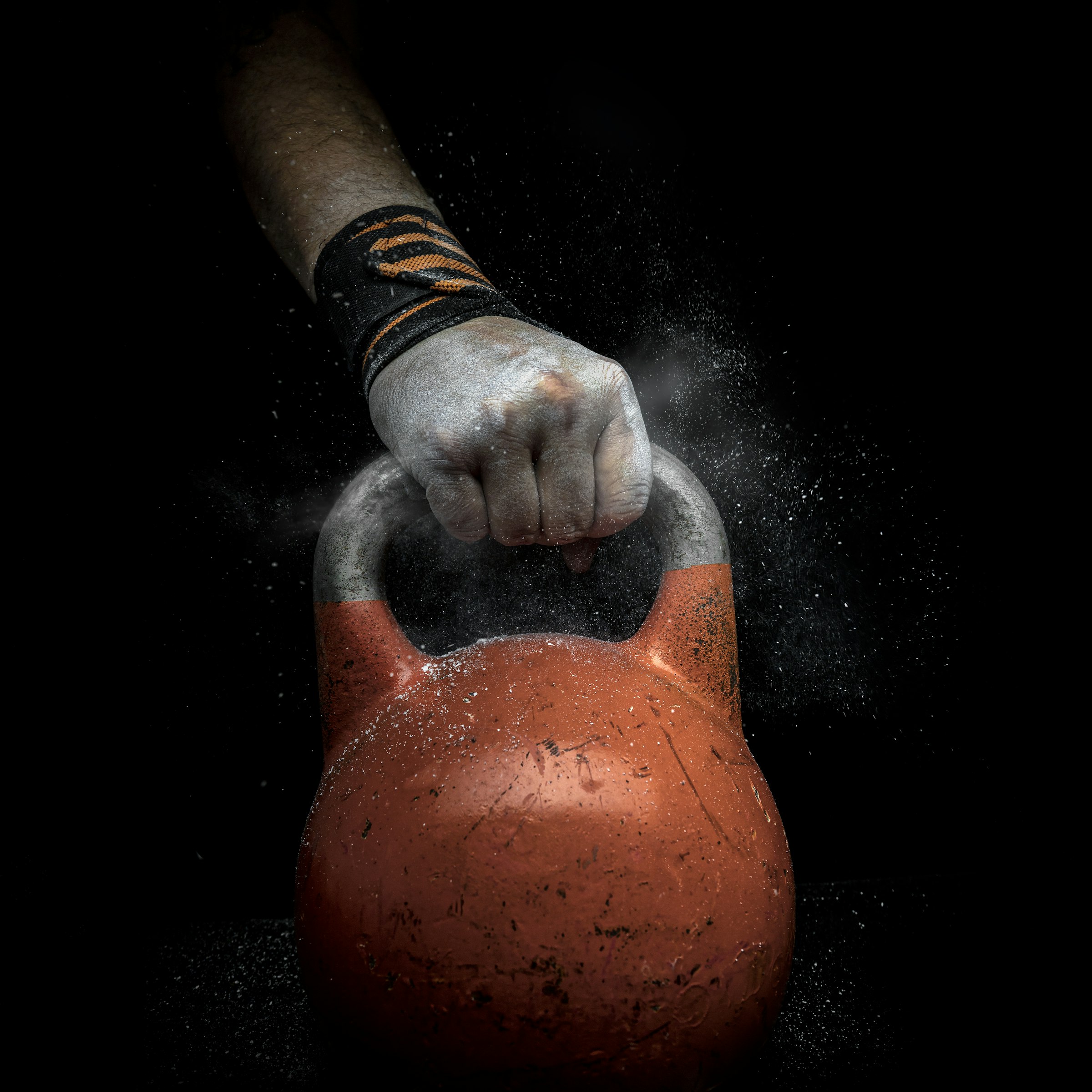 A chalked hand lifting a kettlebell, with chalk dust in the air