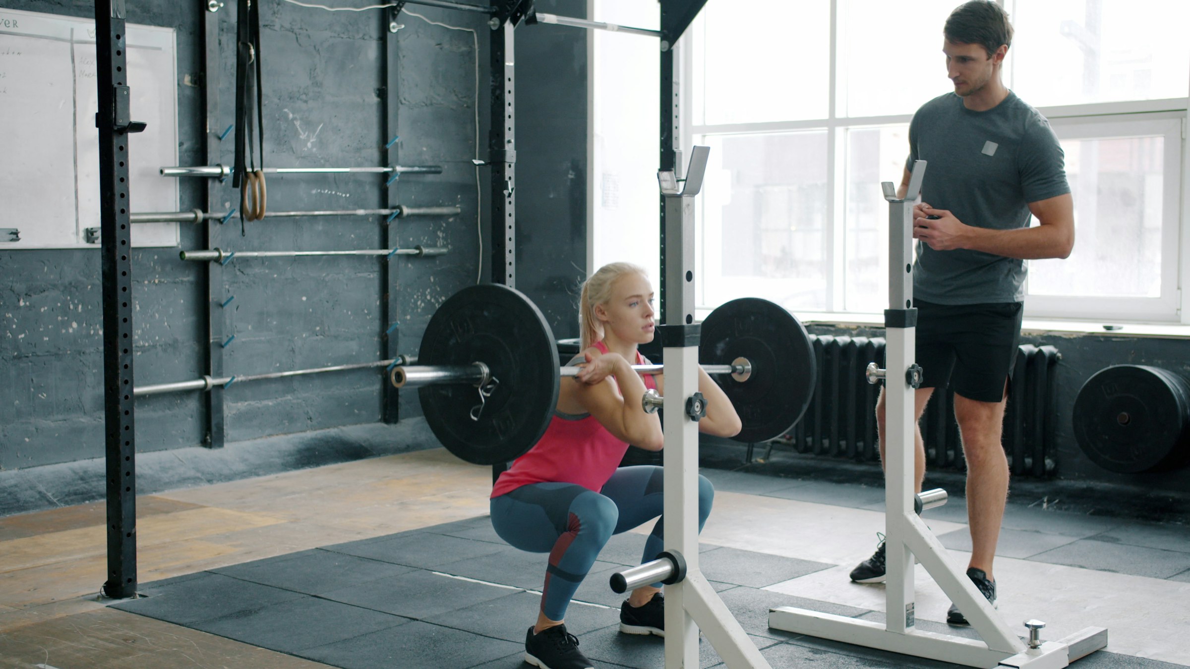 A person squatting with a barbell while another person watches their form