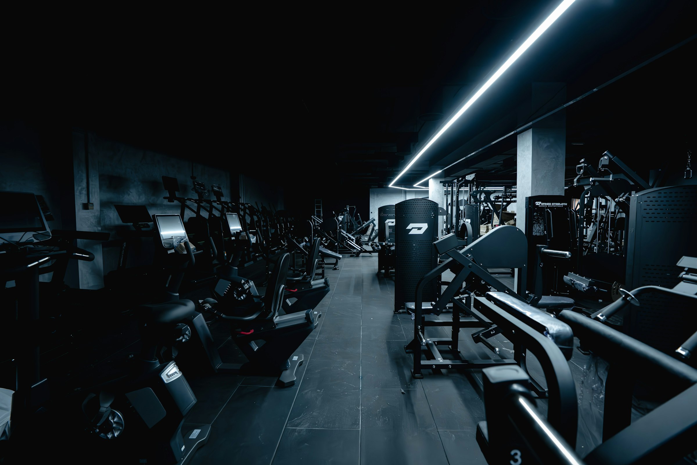 Rows of training machines in a dark gym under a strip light