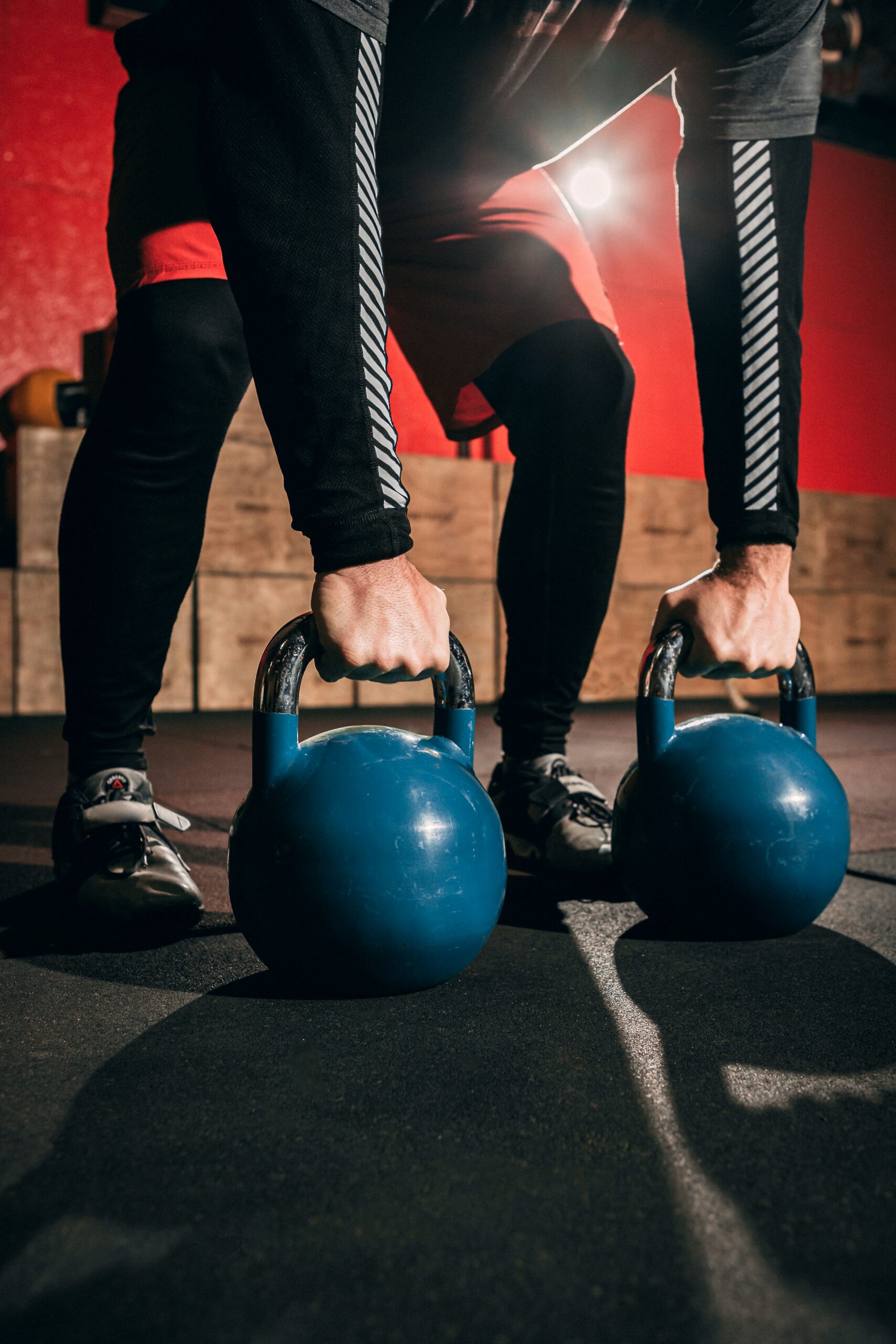 Two hands gripping a pair of blue kettlebells