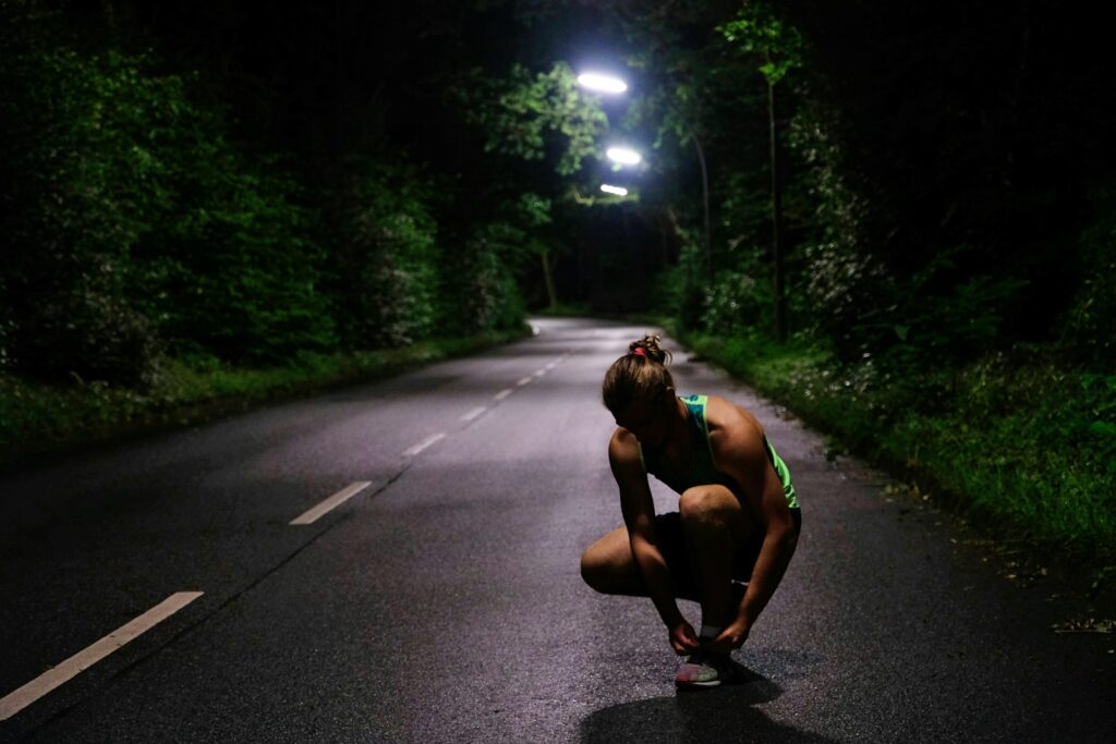 A runner crouched to tie a shoe on a road at night