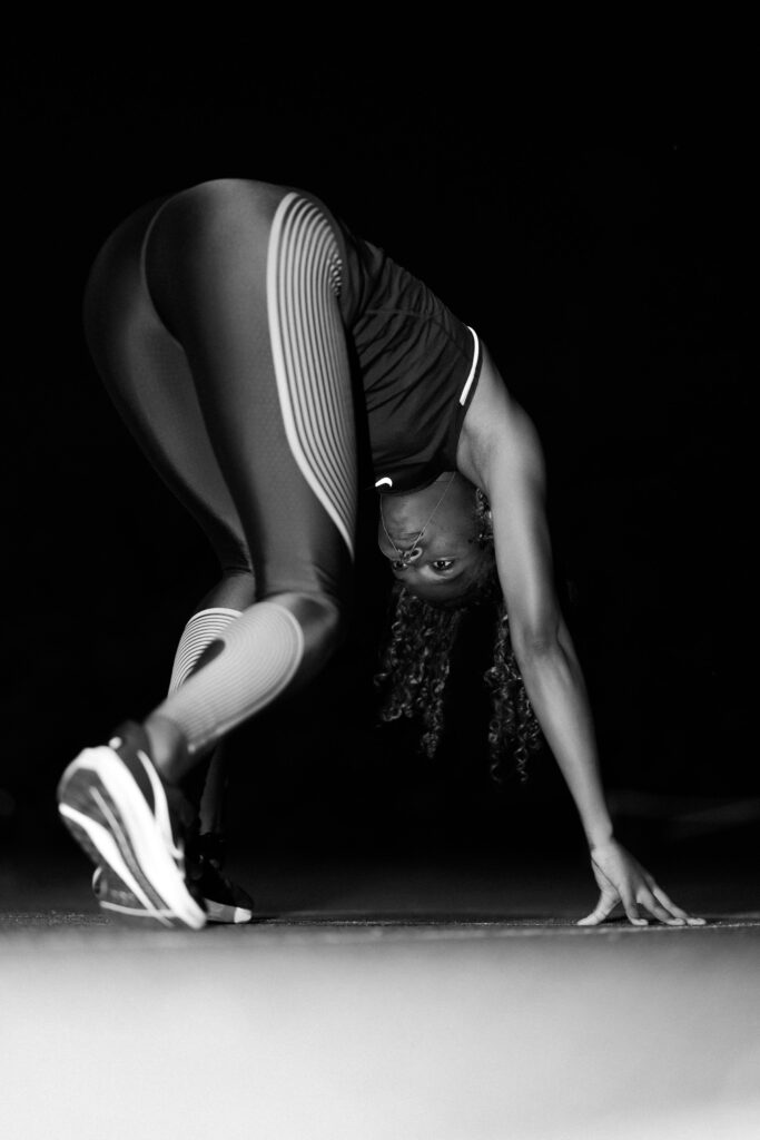 An athlete low in a stretched start position, in black and white